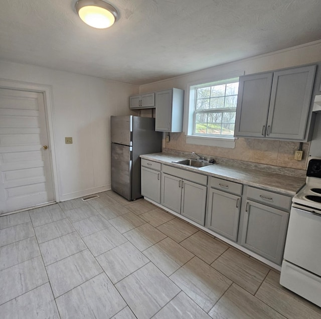 kitchen featuring a sink, white electric range, backsplash, gray cabinetry, and freestanding refrigerator