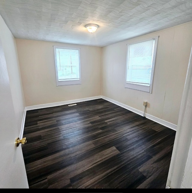 empty room featuring baseboards, dark wood-style flooring, and visible vents