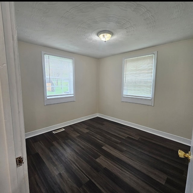 unfurnished room with dark wood finished floors, a textured ceiling, baseboards, and visible vents