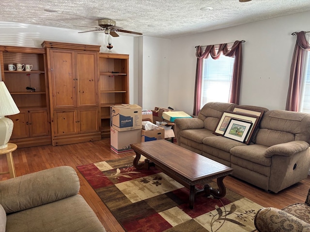 living room featuring ceiling fan, light wood-type flooring, and a textured ceiling