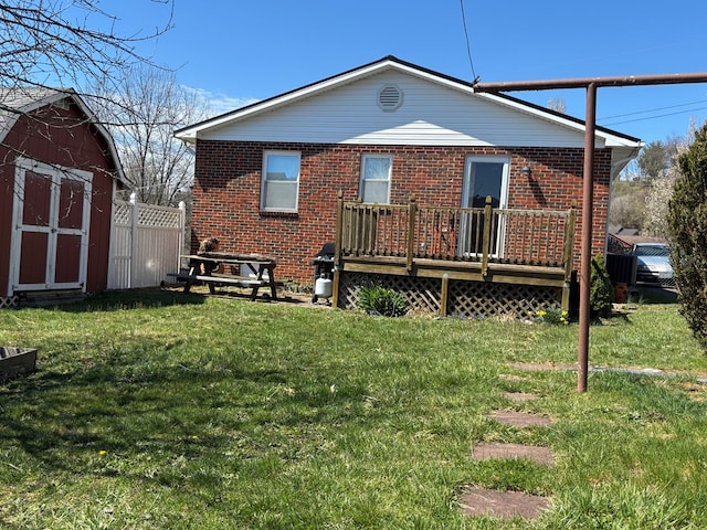 back of property featuring brick siding, a shed, a deck, an outbuilding, and a lawn