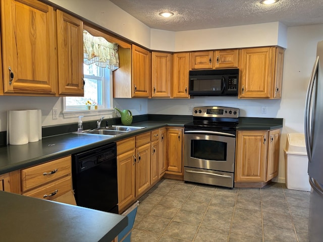 kitchen with dark countertops, a sink, a textured ceiling, brown cabinetry, and black appliances