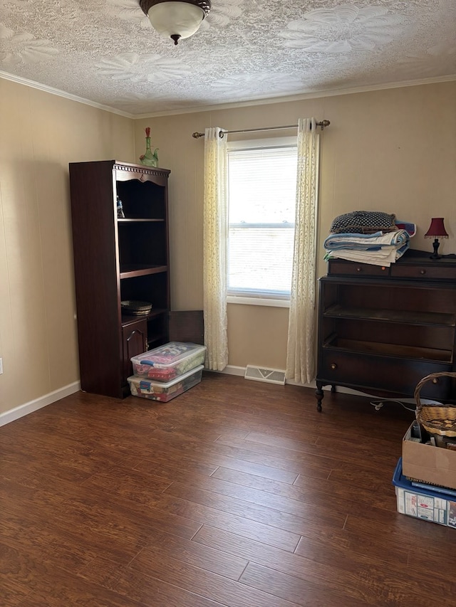 interior space with a textured ceiling, baseboards, wood finished floors, visible vents, and ornamental molding