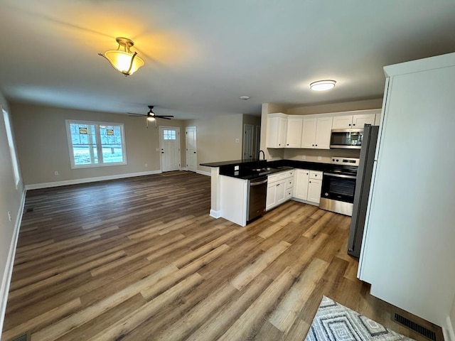 kitchen featuring dark countertops, open floor plan, stainless steel appliances, white cabinets, and a peninsula