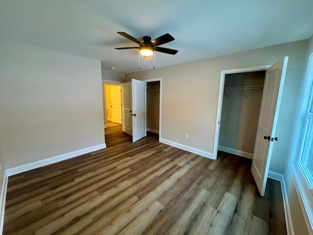 unfurnished bedroom with wood finished floors, baseboards, two closets, and a ceiling fan