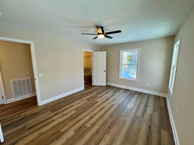 unfurnished bedroom with a walk in closet, wood finished floors, visible vents, and baseboards