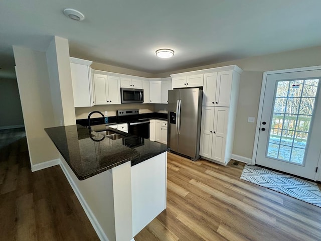 kitchen featuring stainless steel appliances, a sink, light wood-style floors, baseboards, and a peninsula