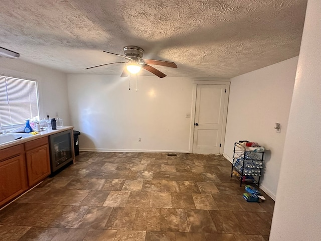 interior space with brown cabinetry, a ceiling fan, a sink, beverage cooler, and baseboards