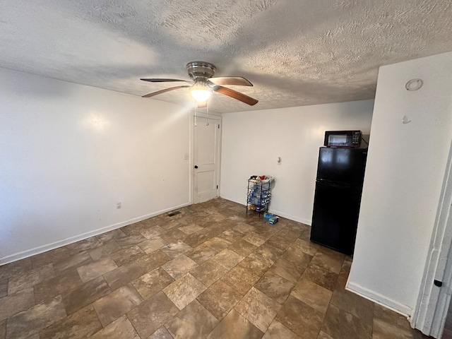 empty room with stone finish flooring, a textured ceiling, baseboards, and a ceiling fan