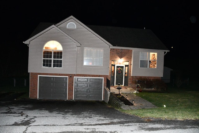raised ranch with a lawn, brick siding, aphalt driveway, and a garage