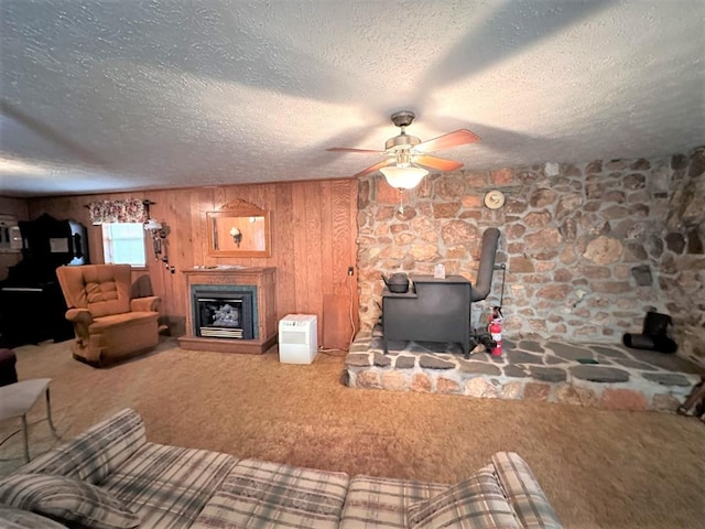 542 Volunteer Rd, Fancy Gap, VA 24328 - carpeted living room featuring a wood stove, ceiling fan, a textured ceiling, a fireplace, and wood walls