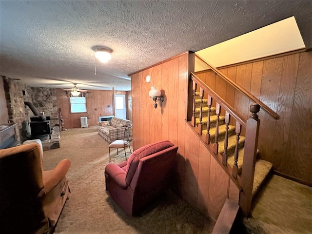 542 Volunteer Rd, Fancy Gap, VA 24328 - carpeted living room with a wood stove, stairs, wood walls, a textured ceiling, and ceiling fan
