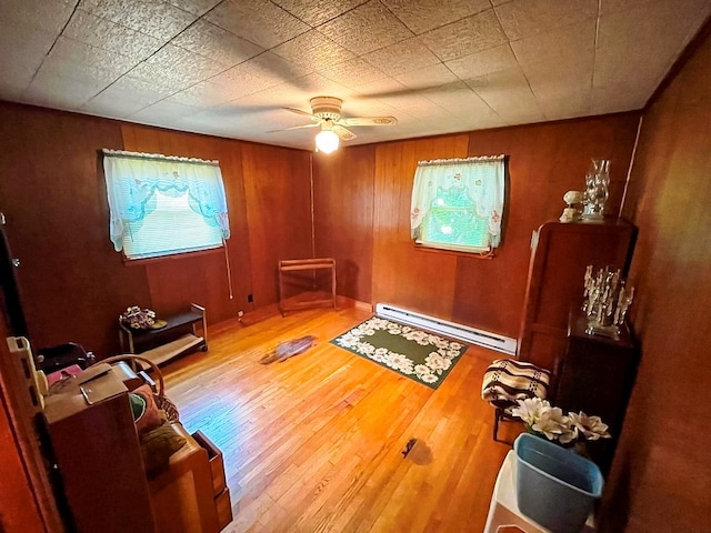 living area featuring a baseboard heating unit, wood walls, hardwood / wood-style floors, and ceiling fan