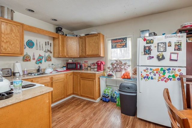 kitchen with sink, stovetop, white refrigerator, a textured ceiling, and light wood-type flooring