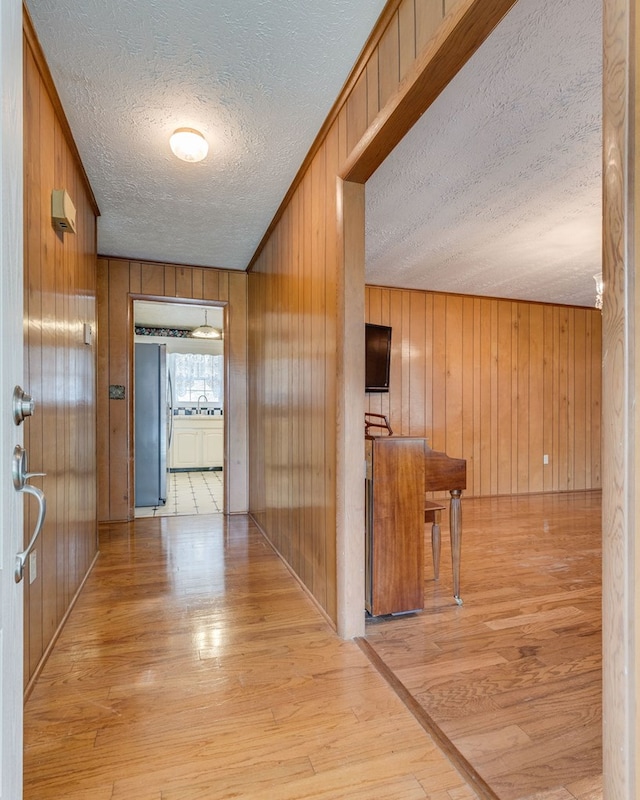 hallway with a textured ceiling, wood walls, and light wood-type flooring