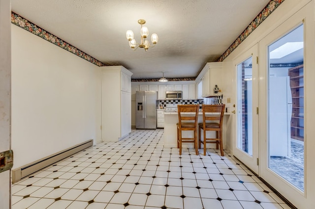 kitchen with white cabinets, a peninsula, stainless steel appliances, light floors, and a baseboard heating unit