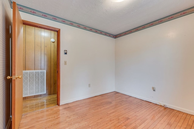 spare room featuring light wood-style floors, baseboards, visible vents, and a textured ceiling