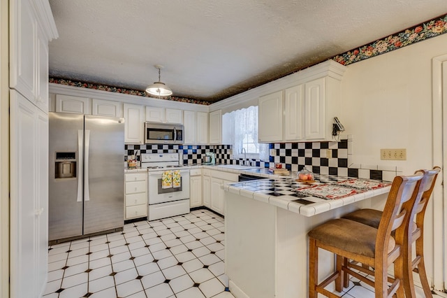 kitchen featuring white cabinets, tile countertops, a peninsula, stainless steel appliances, and a sink