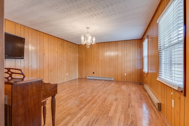 spare room featuring a chandelier, baseboard heating, a textured ceiling, and light wood-style flooring