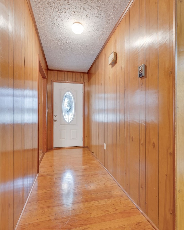 doorway to outside with a textured ceiling, light wood finished floors, and wood walls