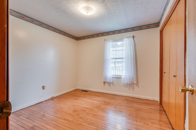 unfurnished room with a textured ceiling, light wood-style flooring, visible vents, and baseboards