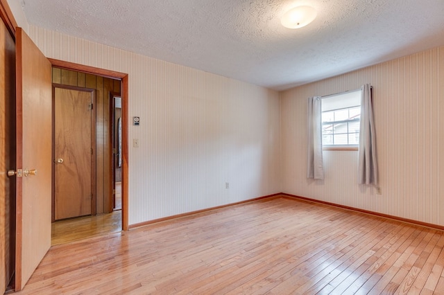 unfurnished room with a textured ceiling, light wood-style flooring, and baseboards