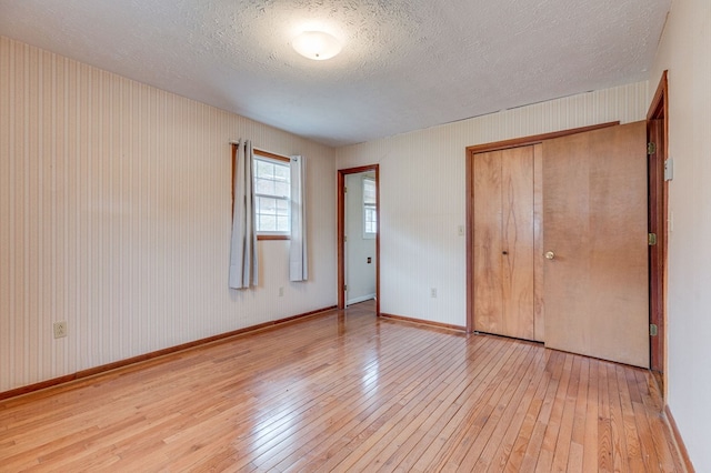 unfurnished bedroom with a closet, a textured ceiling, baseboards, and hardwood / wood-style flooring