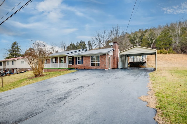 single story home featuring driveway, brick siding, a chimney, a front lawn, and a detached carport