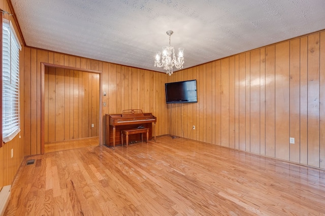 spare room featuring visible vents, an inviting chandelier, wood walls, a textured ceiling, and wood finished floors