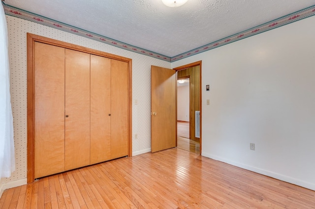 unfurnished bedroom with a textured ceiling, light wood-style flooring, visible vents, baseboards, and wallpapered walls