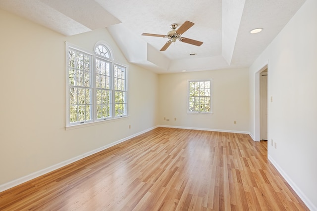 unfurnished room with light wood-style floors, a ceiling fan, baseboards, and a tray ceiling