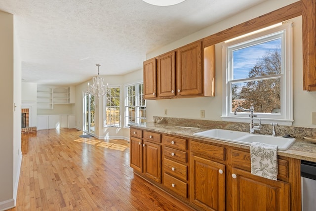 kitchen with brown cabinets, an inviting chandelier, a sink, a textured ceiling, and light wood-type flooring