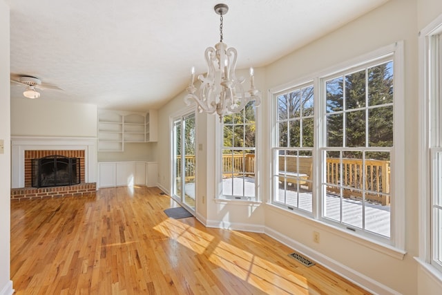 unfurnished dining area featuring visible vents, a fireplace, wood finished floors, baseboards, and a notable chandelier