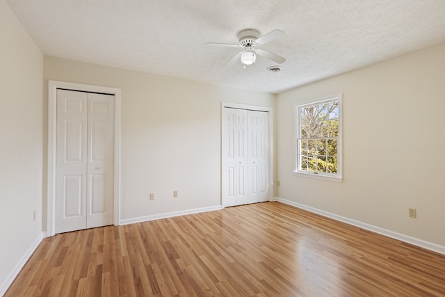 unfurnished bedroom featuring baseboards, two closets, light wood-type flooring, and visible vents