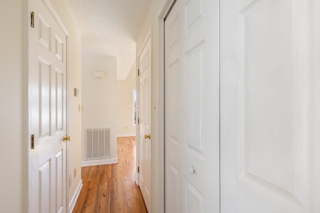 corridor featuring baseboards, light wood-type flooring, a textured ceiling, and visible vents