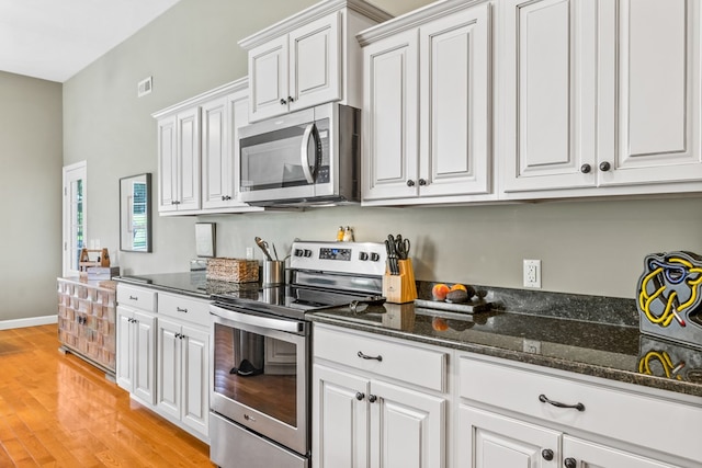 kitchen with appliances with stainless steel finishes, white cabinets, light wood-type flooring, and dark stone counters