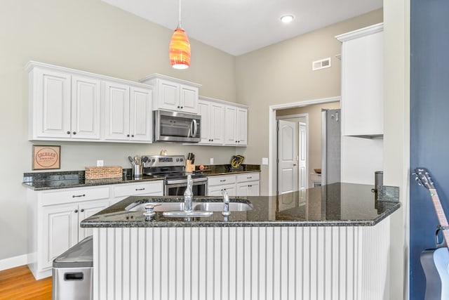 kitchen featuring white cabinetry, stainless steel appliances, kitchen peninsula, and dark stone countertops