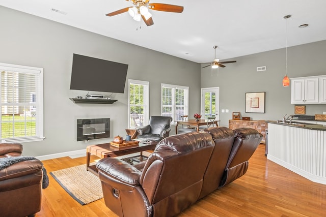 living room with ceiling fan, plenty of natural light, a towering ceiling, and light wood-type flooring