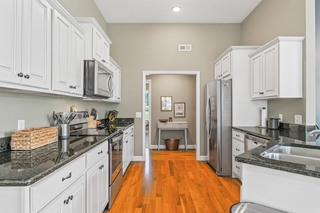 kitchen featuring sink, appliances with stainless steel finishes, white cabinets, dark stone counters, and light wood-type flooring