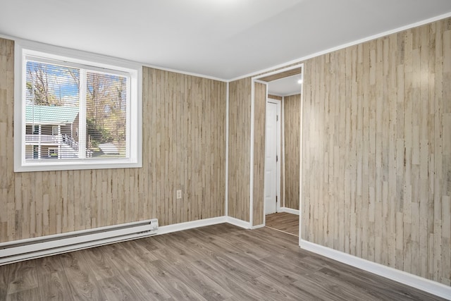 spare room with a baseboard heating unit, wood finished floors, wood walls, and baseboards