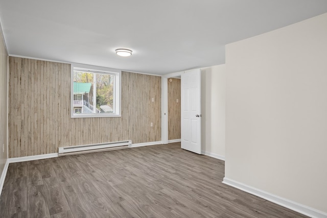 unfurnished room with a baseboard heating unit, wood finished floors, baseboards, and wood walls