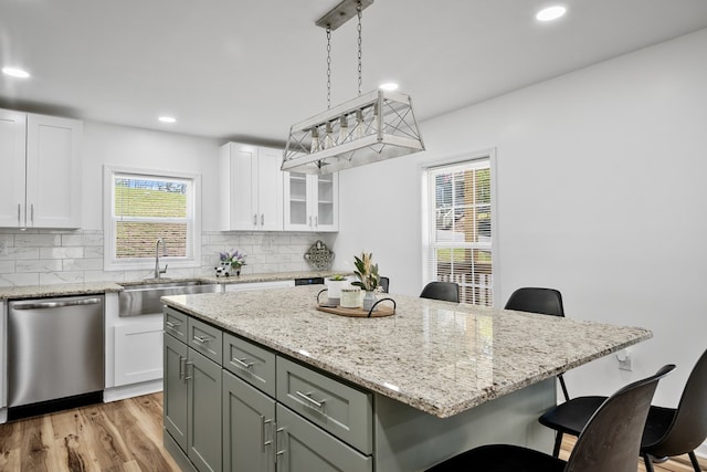 kitchen featuring dishwasher, a sink, a kitchen bar, white cabinetry, and recessed lighting