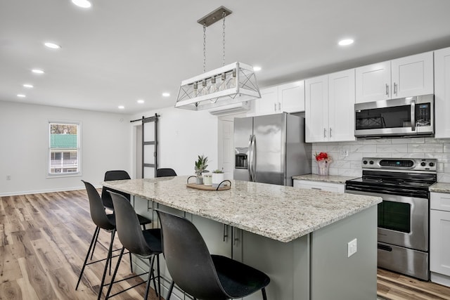 kitchen featuring stainless steel appliances, a barn door, a kitchen island, light stone counters, and recessed lighting