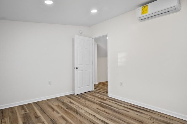 unfurnished room with a wall mounted AC, wood finished floors, recessed lighting, and baseboards
