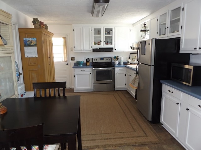 304 Edgewood Dr, Galax, VA 24333 - kitchen with stainless steel appliances, under cabinet range hood, dark countertops, white cabinetry, and glass insert cabinets