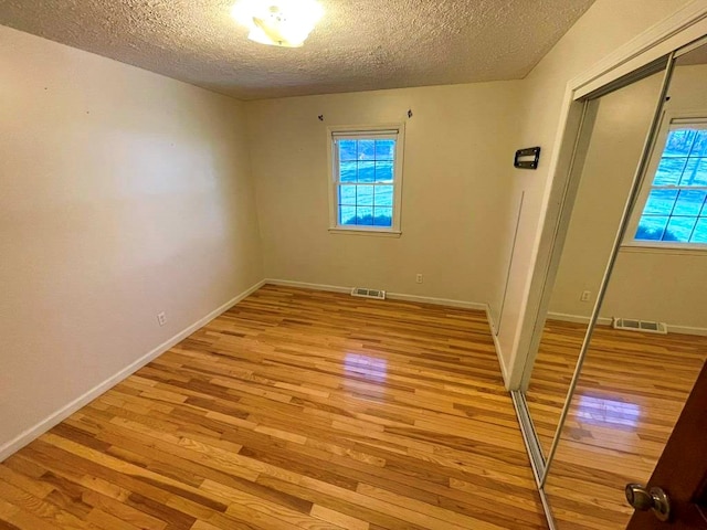 empty room with a textured ceiling, a healthy amount of sunlight, and light wood-type flooring