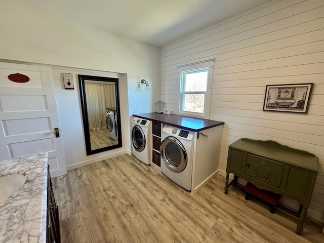 washroom featuring sink, light hardwood / wood-style floors, washer and dryer, and wood walls