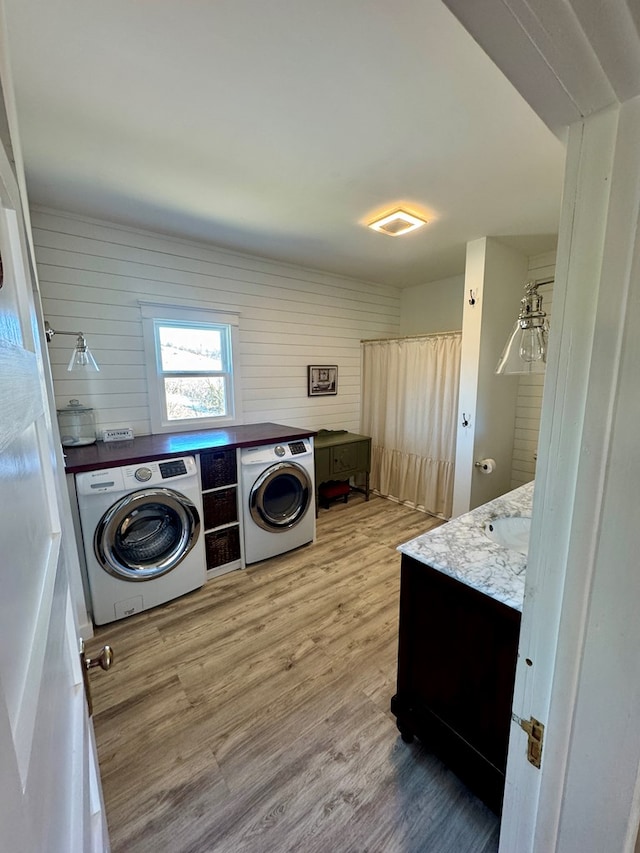 clothes washing area with washing machine and dryer, sink, and light hardwood / wood-style flooring