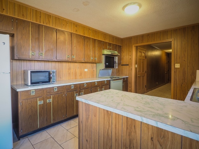 kitchen featuring light countertops, white appliances, a textured ceiling, wooden walls, and under cabinet range hood