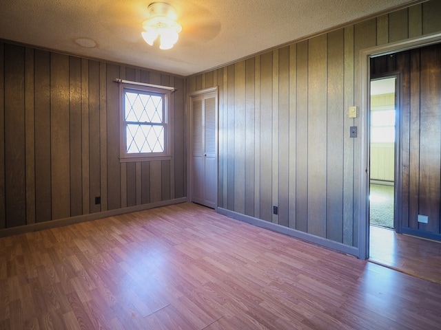 empty room with wooden walls, ceiling fan, wood finished floors, and a textured ceiling